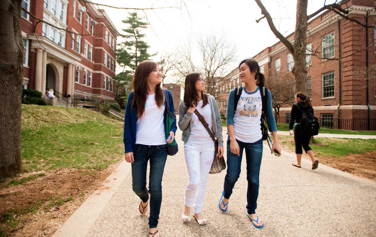 students with backpacks walk on campus sidewalks
