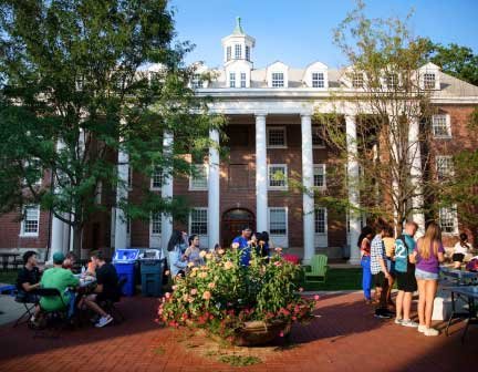 students stand in front of a tall brick building with columns 