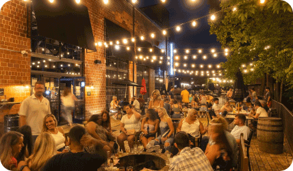 people sit at tables outside under string lights