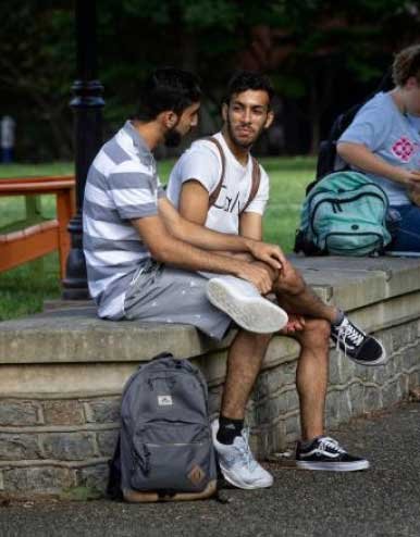 two students sit on a brick wall lining a sidewalk