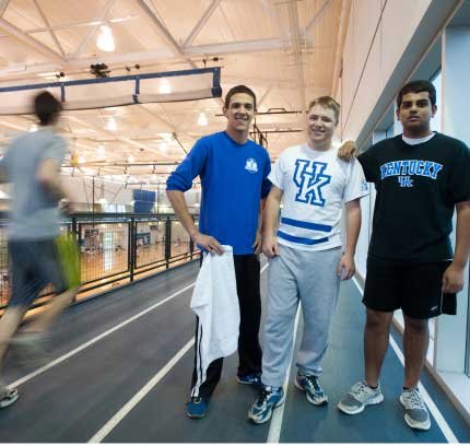 Three male students pose in a large gymnasium
